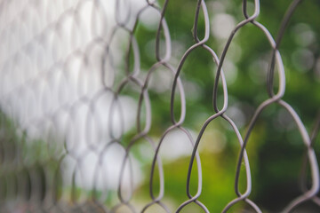 Close up picture of fence net on green background. Metallic net, as protection in the garden. Barrier on the guard, as background. Steel mesh in the yard.