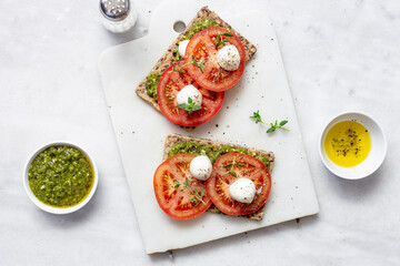 Mozzarella cheese, tomatoes and  pesto bruschetta on light marble background, top view. Pesto and...
