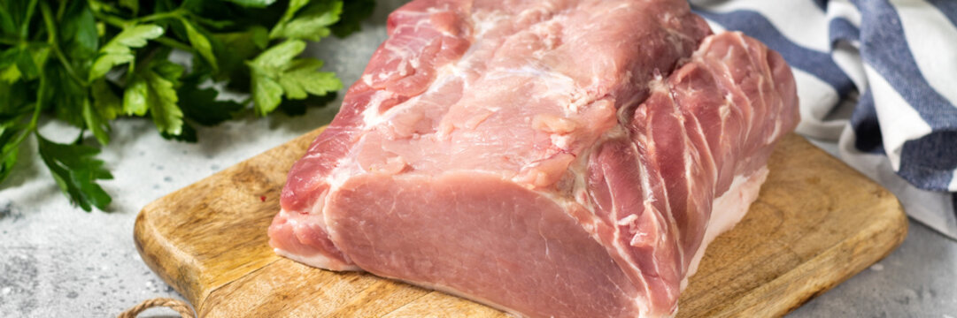 Raw pork carbonate on a white ceramic plate on the light gray kitchen table. Raw pork meat, tenderloin. Banner	
