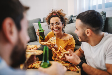 Group of best friends having pizza party at home. They are chatting, eating pizza and drinking beer.