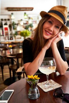 Young happy cute white woman in hat drinking gin tonic cocktail in cafe restaurant