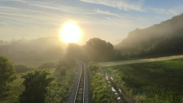 Drone fly over a railroad truck in the natural green forest with the sun on the clear blue sky during a foggy and misty cloudy sunrise