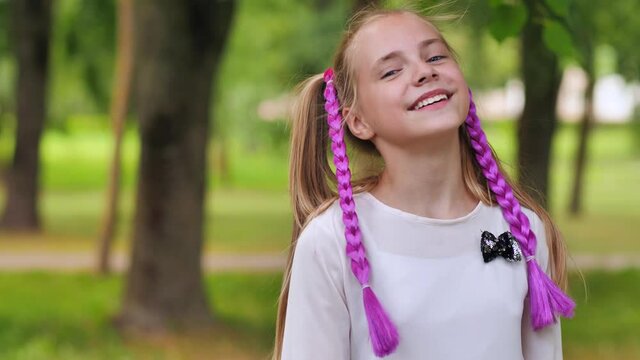 Portrait of a funny girl with pigtails and purple bows in the park.