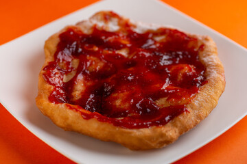 Traditional Transylvanian hungarian pastry, deep fried dough langos with jam close up on white plate