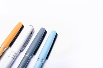 Four pens of blue, white, orange and gray are on a white background from above, from the side, at an angle. Four pens in close-up on a white background. Caps from pen