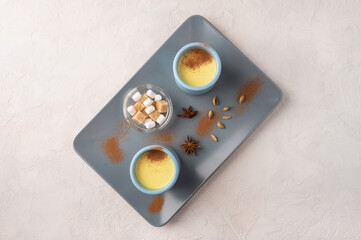 Two blue cups with traditional Indian masala chai tea with spices and sugar on a ceramic tray on a light background. Top view with copy space