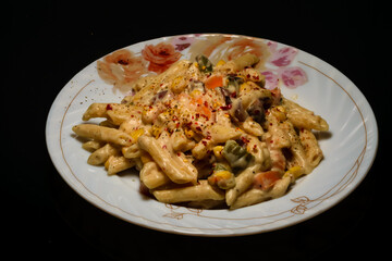 Pasta with white sauce and cheese placed in a plate in a dark background