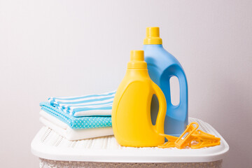 a stack of colored laundry, drying clamps and washing gels in yellow and blue bottles on a white plastic basket for dirty laundry, copy space