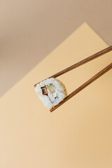 Sushi rolls with chopsticks on a beige and brown background. Stylish composition with sushi.