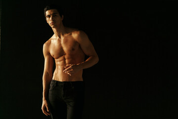 Frontal portrait of an athletic man with a shirtless tanned torso. Studio shoot. Warm dark color.