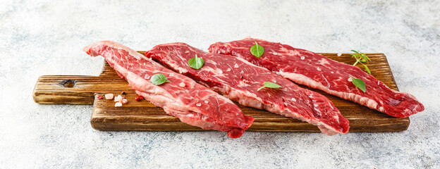 Raw steak with spices on wooden cutting board