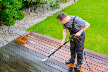 power washing - man cleaning terrace with a power washer - high water pressure cleaner on wooden terrace surface - obrazy, fototapety, plakaty