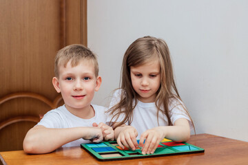 a boy and a girl of European appearance in light clothng sit and play a Board game