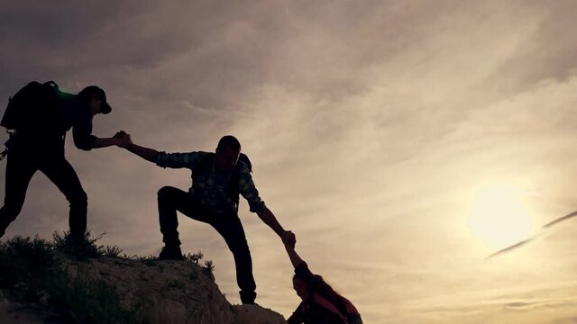 Teamwork of the business group. Male partners climb to the top. Silhouette of a helping hand at sunset. The concept of travel, extreme sports, winning business.