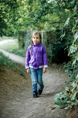 a girl in a light purple jacket with two pigtails is walking along a path among the greenery