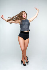 A young fashionable woman with long hair in short shorts is dancing. Not a thin girl in fishnet tights dancing in high heels. Posing for the camera.