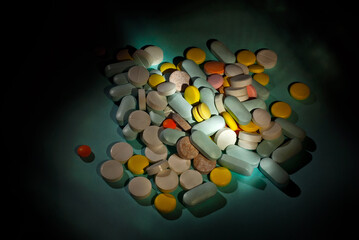 White, yellow, red, orange and blue pills on a cardboard background. Medication on a dark background with contrasting dramatic light.