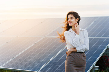 Model with solar panels stands in row on the ground at sunset. Girl dressed white formal shirt smiles on the power plant. Free electricity for home. Green energy. Solar cells power plant business.