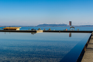 Obraz premium The reflection of the sky on the water surface of the basin prolongs the reflection of Lake Neuchatel. In the background, the snow-covered peaks of the Alps can be seen.