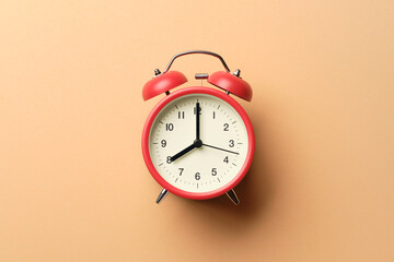 Red vintage alarm clock on pastel orange paper background.