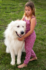 a sweet smiling girl of seven with her friend a Maremma dog on a green lawn
