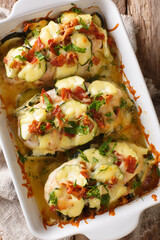 Summer food baked chicken fillet with zucchini, bacon and cheese close-up in a baking dish. vertical top view