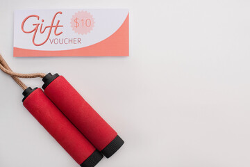Top view of skipping rope near gift voucher with 10 dollars sign on white background