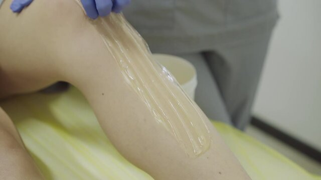 Applying a sugar paste and removing it from female leg on couch