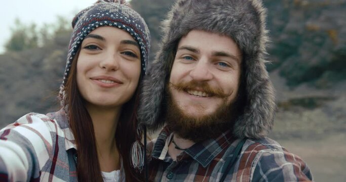 Young hypster couple takes a video of themselves standing on the top of a rock with beautiful mountain view behind