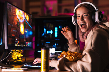 Image of excited cute girl eating chips while playing video game