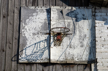 An old, abandoned and damaged basketball board with a hoop and net in a countryside.