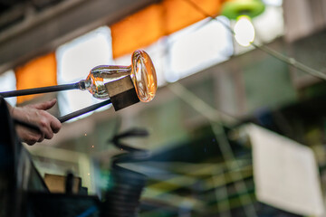 Close-up on the hand of a glassblower artist shaping the molten glass extracted from the furnace in...