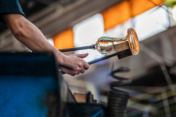 Caucasian glassblower artist is shaping the molten glass extracted from the furnace located in a glass factory in Romania where each piece is manually made by the artisans hands. Labour day.