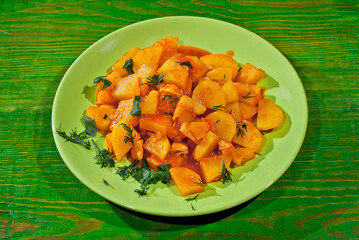 Potatoes with parsley in a green plate on a wooden table. Boiled potatoes with orange sauce. Food in utensils on the background of an old shabby board.