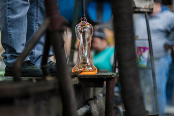 Beautiful close-up shot of glassblower craftsman artist's shaping the piece of molten glass in his workshop. Art and crafts.