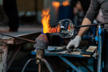 Close-up of a glassblower artisan shaping the hot molten glass at strong fire inside his workshop. Manual glass processing by the craftsmen inside a glass factory in Transylvania, Romania.