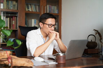adult Asian businessman working from home serious and thinking