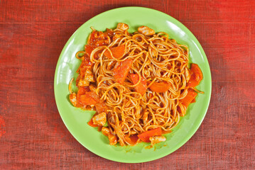 Pasta with carrots in a green plate on a wooden table. Vermicelli with orange sauce on red plywood. Place for text near the plate. Copy space for design.