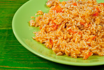 Pilaf with meat and carrots in a green plate. Rice on an old shabby board.