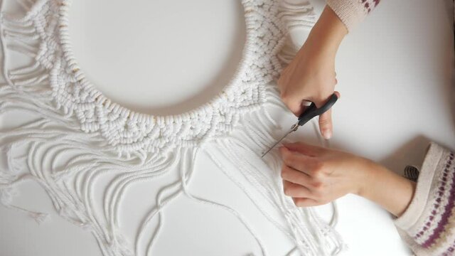 Boho style woman cutting circle wall hanging macrame with scissors on a white table with a yellow light