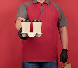 man in a red T-shirt, wearing black latex gloves, holds a tray with disposable cups of coffee