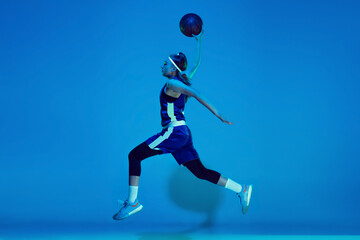 Fototapeta na wymiar Leader. Young caucasian female basketball player training, prcticing with ball isolated on blue background in neon light. Concept of sport, movement, energy and dynamic, healthy lifestyle.
