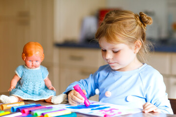 little alone toddler girl painting with felt pens during pandemic coronavirus quarantine disease. Happy creative child with old vintage doll, homeschooling and home daycare with parents