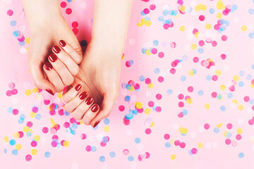 Obraz na płótnie Canvas Manicure and nailcare concept. Two woman hands and falling confetti on pink background. Classic red polish. Flat-lay, top view. 