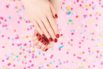 Fototapeta na wymiar Manicure and nailcare concept. Two woman hands and falling confetti on pink background. Classic red polish. Flat-lay, top view. 