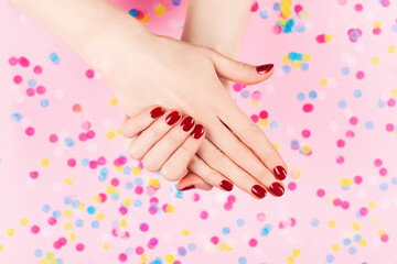 Manicure and nailcare concept. Two woman hands and falling confetti on pink background. Classic red polish. Flat-lay, top view. 
