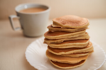 Homemade pancakes are on the table. Nearby is a mug of coffee with milk. Light background