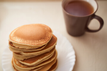 Homemade pancakes are on the table. Nearby is a mug of black tea with milk. Light background