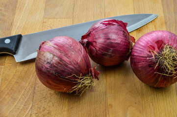 Red Onions on a wooden cutting board with kitchen knife close up, Tropea red onions.