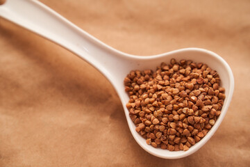 buckwheat lies in a white plastic spoon on a brown background. close up